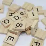 A pile of Scrabble tiles, brown wooden letter blocks on white surface