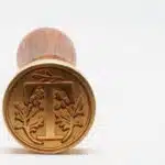 Stamp with letter T on white background, round gold-colored coin on white surface