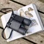 Binoculars rest on a bird identification book open to a page on owls., black binoculars on opened book