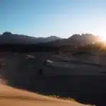 Mesmerizing red sand dunes and endless mountain valleys providing iconic views across NEOM | NEOM, Saudi Arabia, a person is walking in the desert at sunset