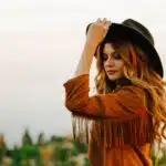 , woman wearing brown jacket with fringe holding hat during daytime