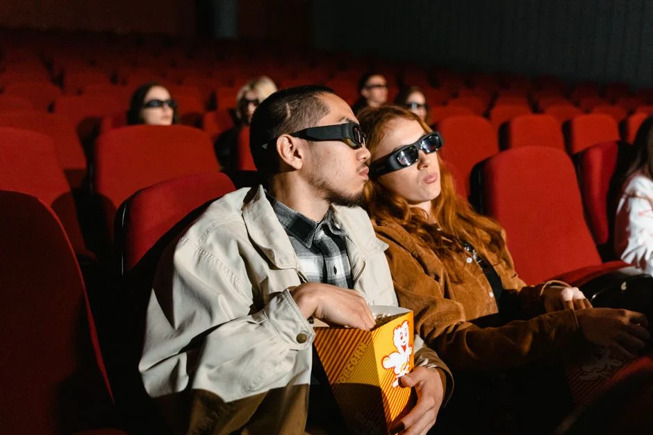 Two moviegoers wearing 3D glasses sharing popcorn in a theater